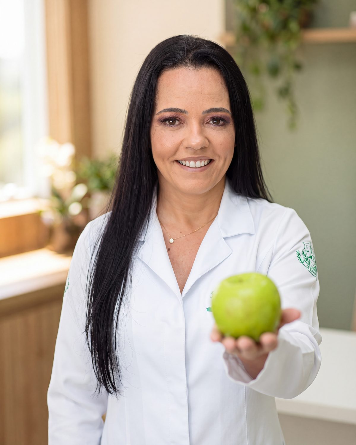 Nutricionista Ismeire Cortez, em Divinópolis-MG, sorrindo de jaleco branco e oferecendo uma maçã verde